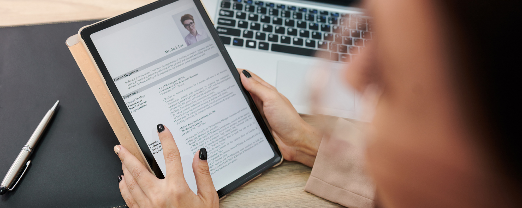 Frau liest Lebenslauf auf E-Reader. Im Hintergrund ein Laptop