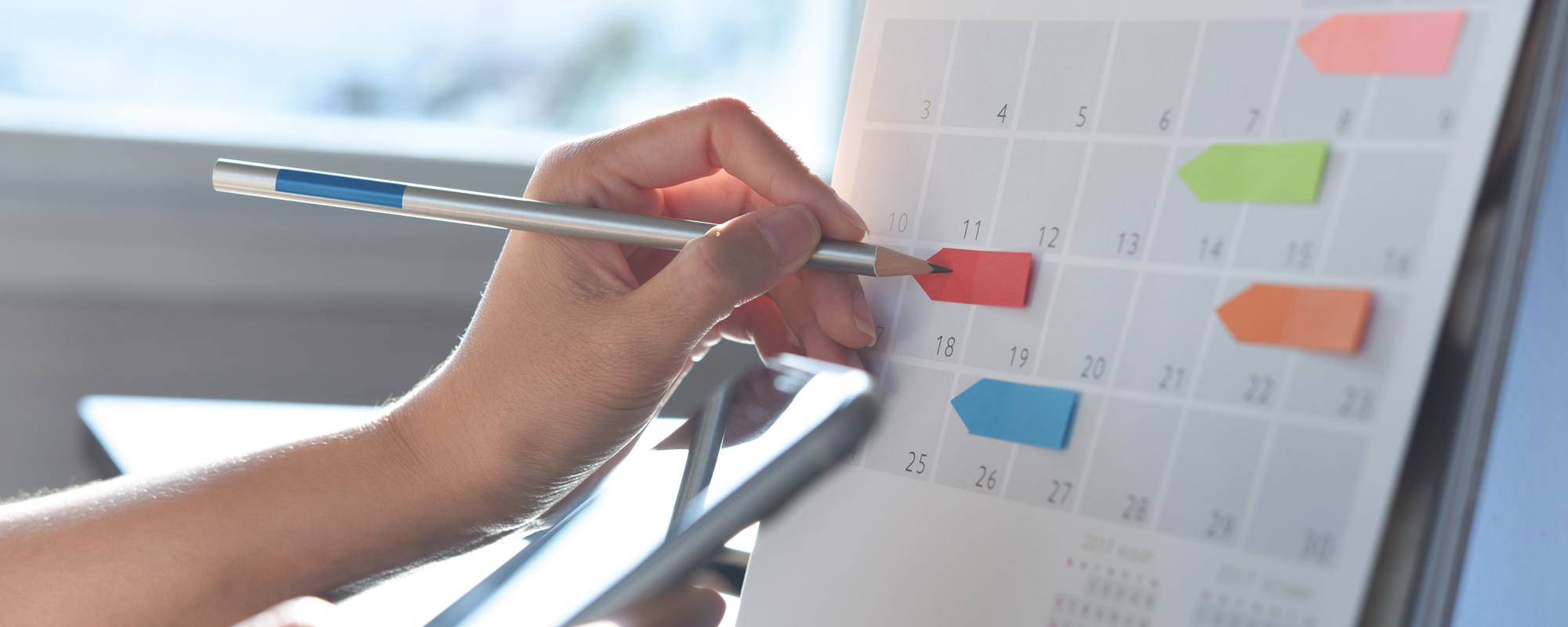 Frau markiert freie Tage in einem großen Wandkalender mit roten und blauen Postits