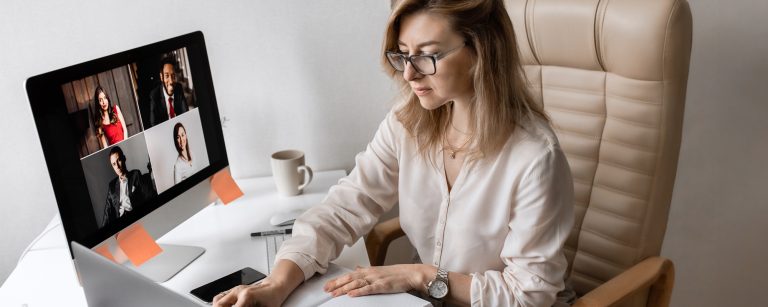 Blonde Frau mit Brille sitzt im Home Office am PC und arbeitet.