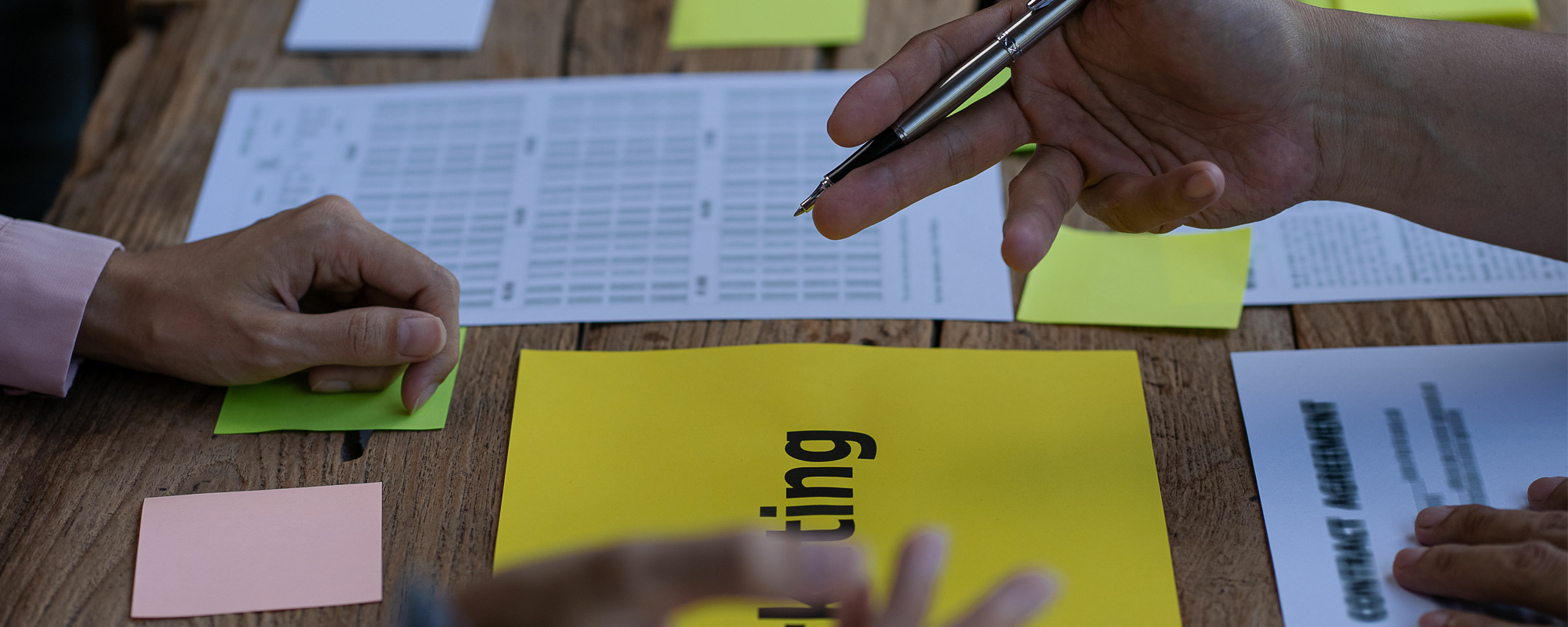 voller Schreibtisch mit ausgedruckten Charts, vielen Postits und arbeitenden Händen.