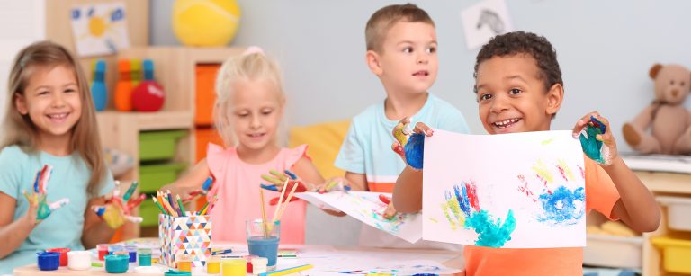 Vier Kinder in einem Kindergarten zeichnen und malen auf einem Tisch.