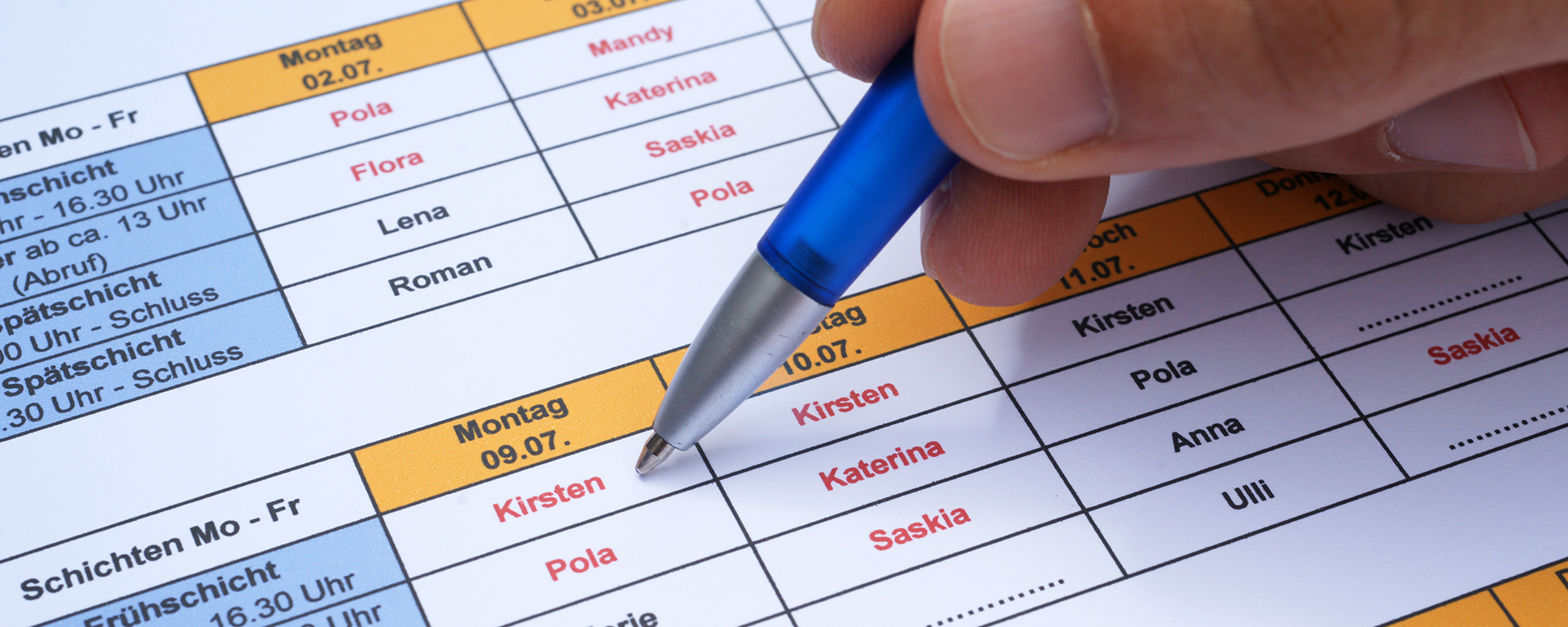 Großer Schichtplan mit Vornamen, Dienstzeiten und einer Hand, die mit Kugelschreiber etwas einträgt-