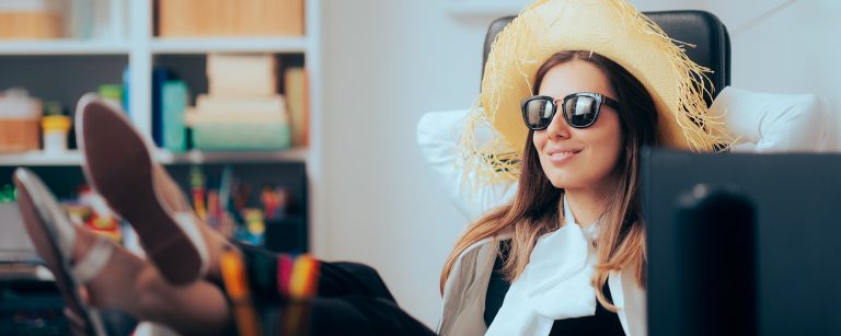 Frau mit Sonnenbrille und riesigem Sonnenhut legt ihre Beine auf den Schreibtisch im Büro und entspannt.