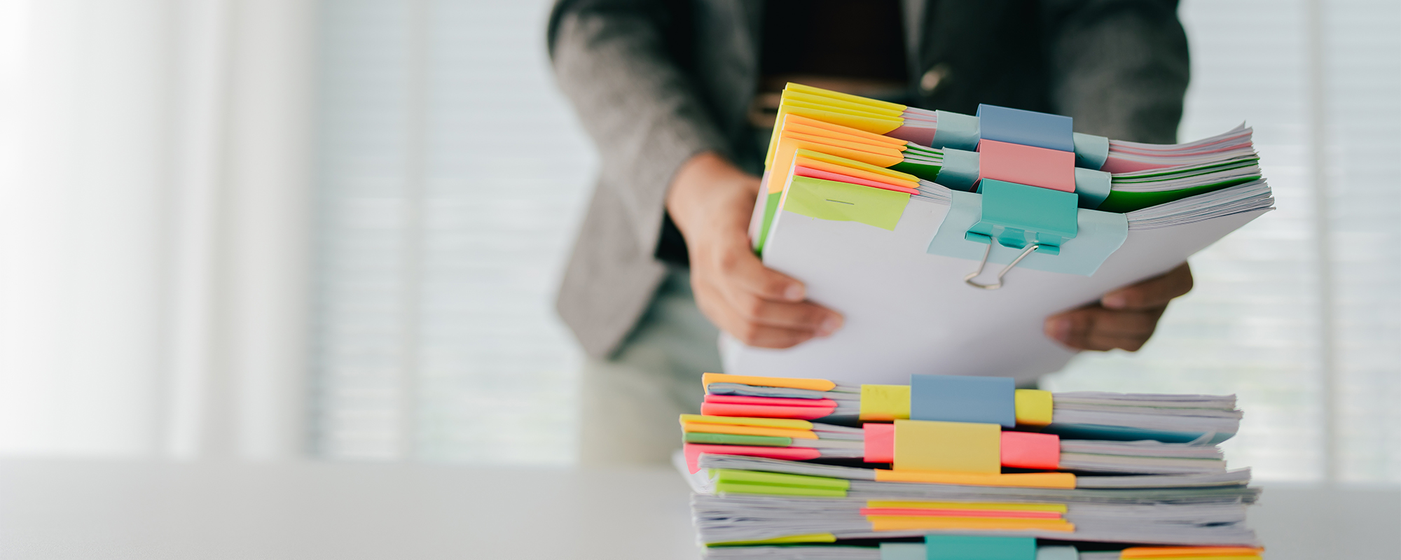 Junge weibliche Büroangstellte ordnet große Aktenstapel auf Schreibtisch.
