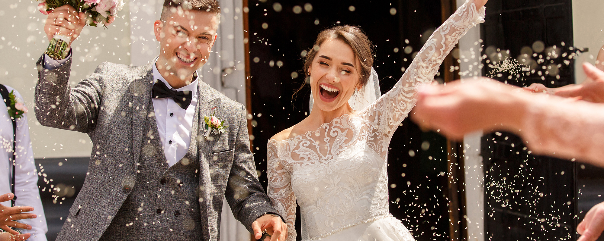 Glücklicher Mann und Frau als Hochzeitspaar nach der Trauung. Freuen sich und werden mit Reis und Getreide beworfen.