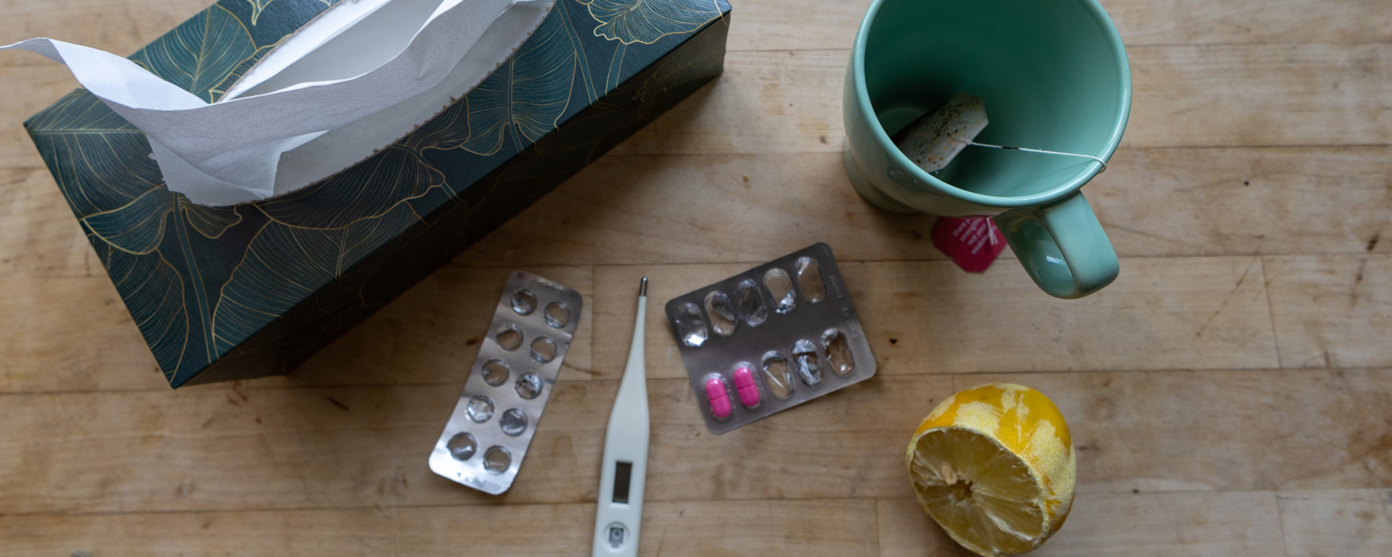 Taschentücher, Tabletten, eine leere Tasse Tee, eine Zitrone und ein Fieberthermometer liegen auf dem Tisch. Symbolbild für einen Krankenstand und welche Daten man seinem Arbeitgeber mitteilen muss.