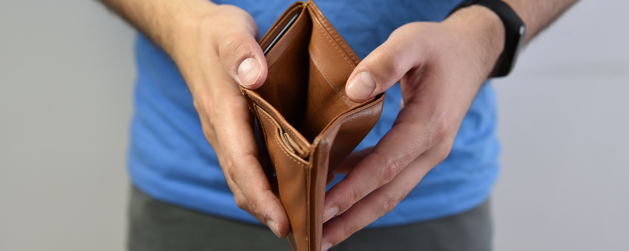 Angestellter zeigt seine leere Brieftasche. Zu hohe Ausgaben und zu niedriges Gehalt für seinen Lifestyle.