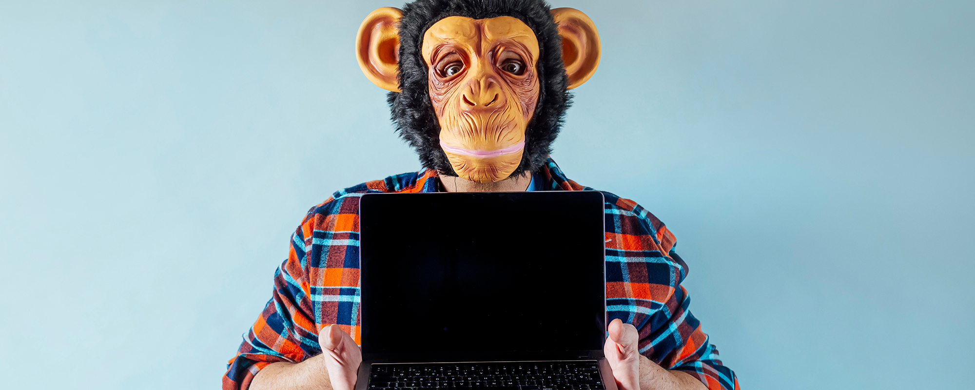 Ein Mann mit einer Affenmaske hält einen Laptop hoch. Das Bild symbolisiert Monkey Work, einfache, repetitive Aufgaben am Computer, im Gegensatz zu anstrengender Donkey Work.