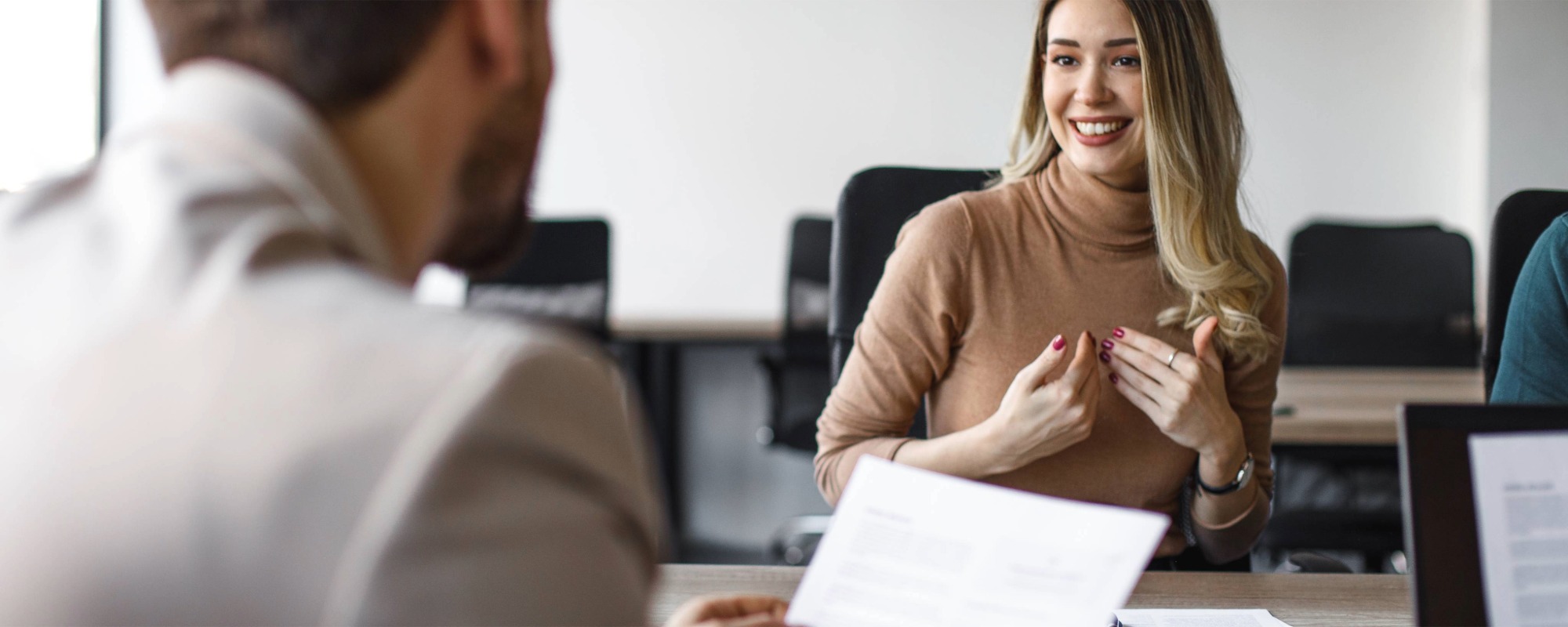 Trickfragen kein Problem: Blonde Frau reagiert beim Bewerbungsgespräch souverän auf schwierige Fragestellungen und überzeugt dadurch den Recruiter im weißen Hemd.