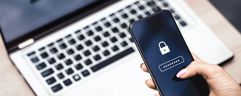 Frau mit rosarotem Nagellack entsperrt ein Handy durch die Eingabe eines gut geschützten Passworts über einem Laptop im Büro.